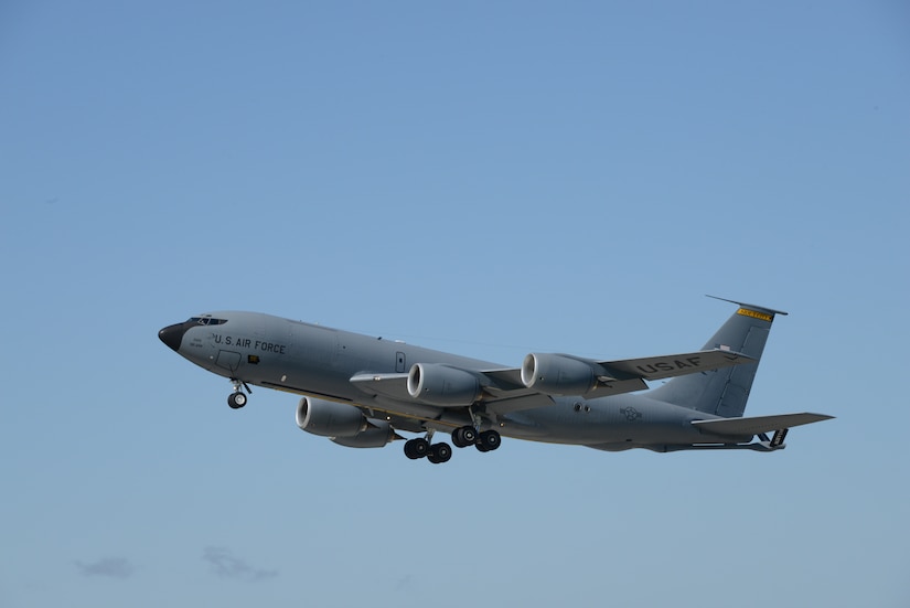 A military aircraft flies against a blue sky.