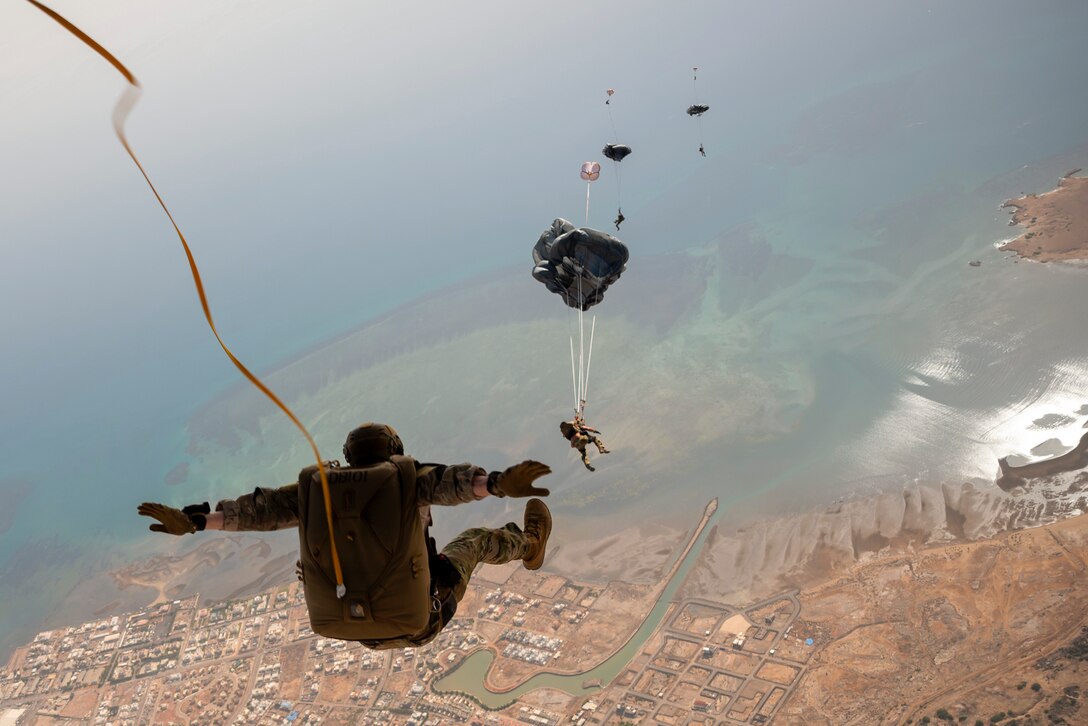 Airmen free fall over a city near a body of water.
