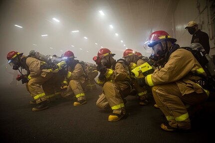 Hose teams of Sailors fight a simulated fire while another Sailor checks for hot spots with a thermal imager in the hangar bay during a general quarters training evolution aboard the Nimitz-class aircraft carrier USS Harry S. Truman (CVN 75) during sea trials after completing an extended carrier incremental availability.