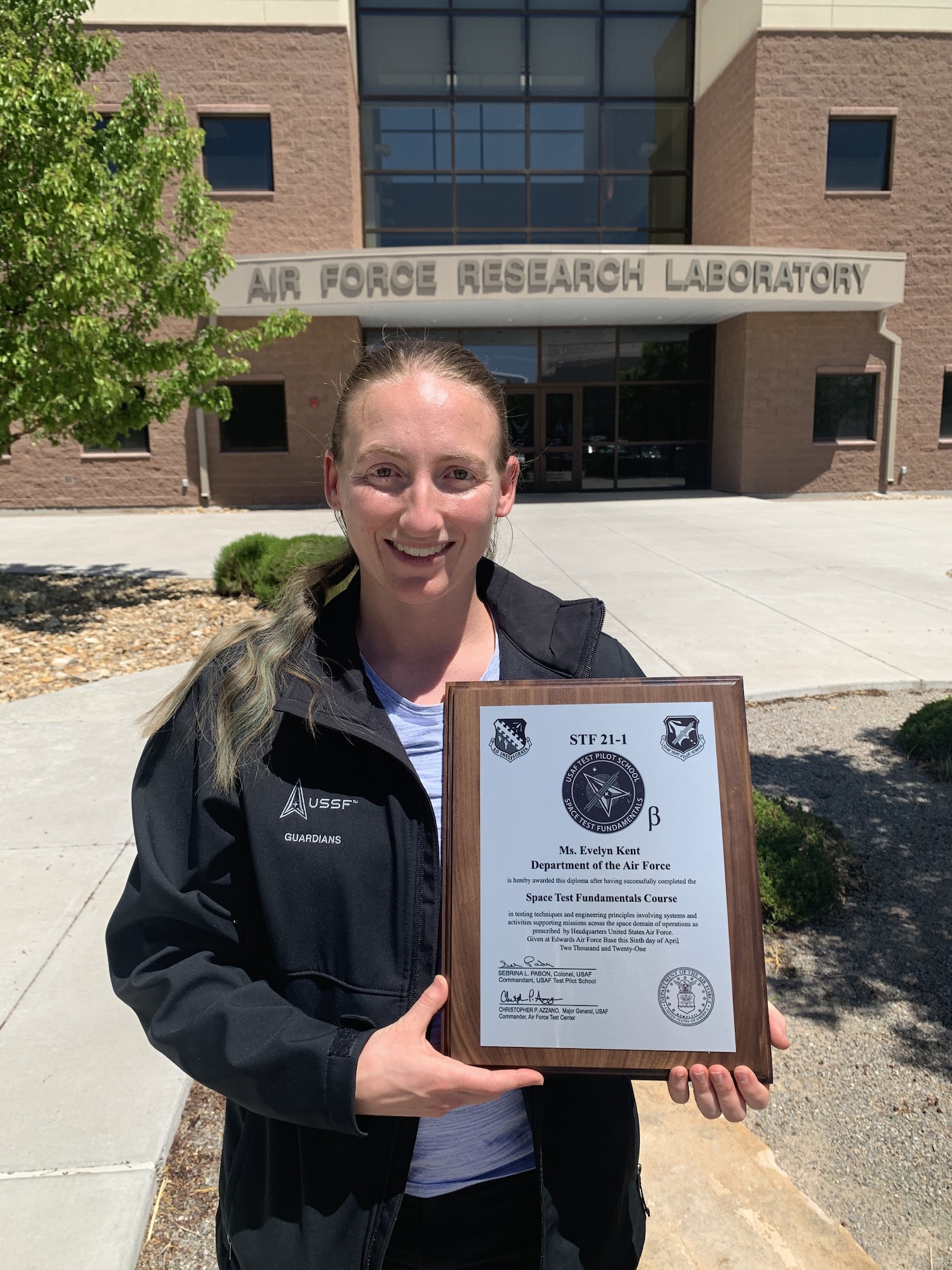 Air Force Research Laboratory engineer Evelyn Kent holds her Space Test Fundamentals course diploma with the AFRL Space Vehicles Directorate headquarters at Kirtland AFB, N.M in the background. Kent graduated from the inaugural space test course earlier this year. (Courtesy photo)