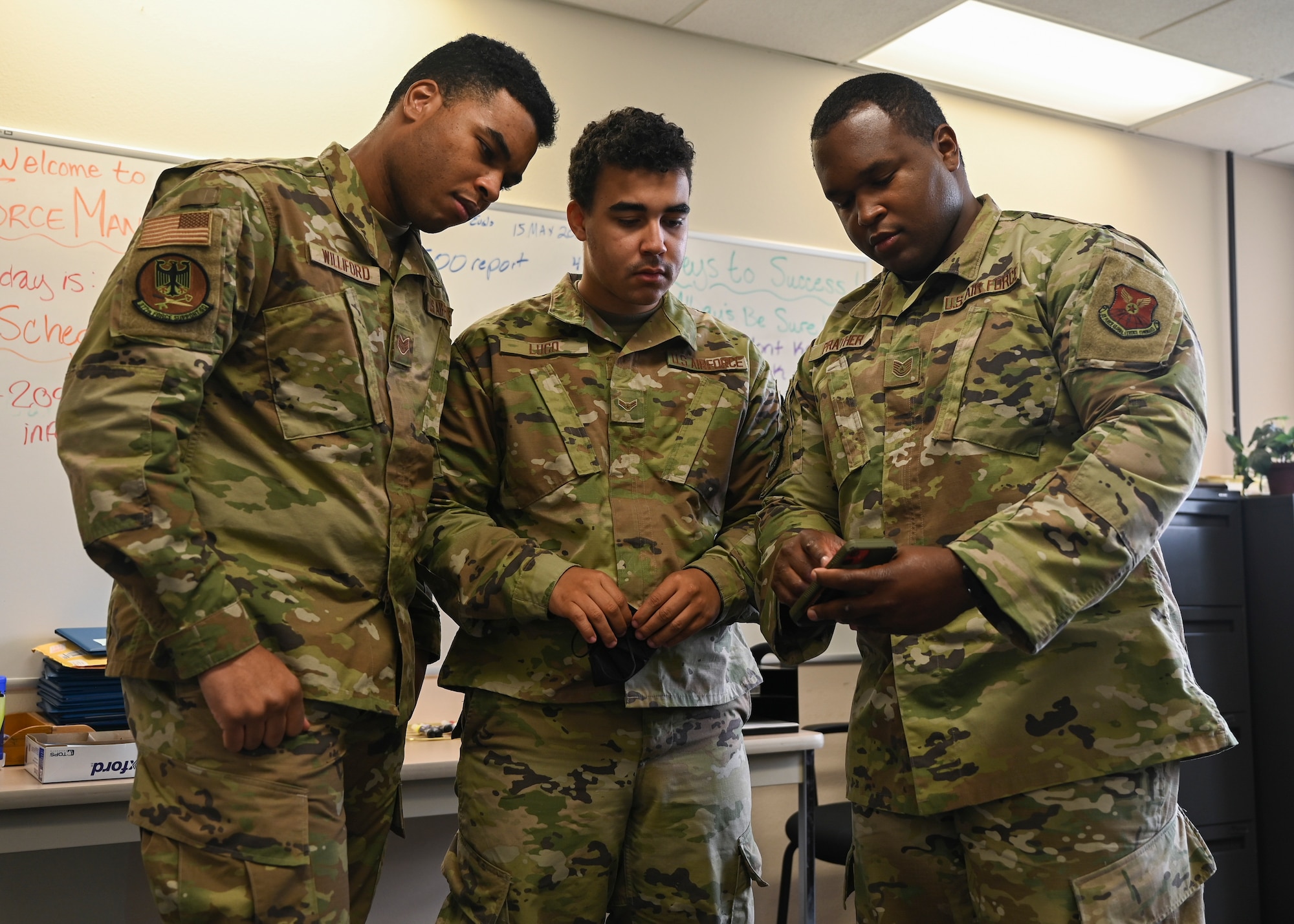 Airmen look at a program on a phone.