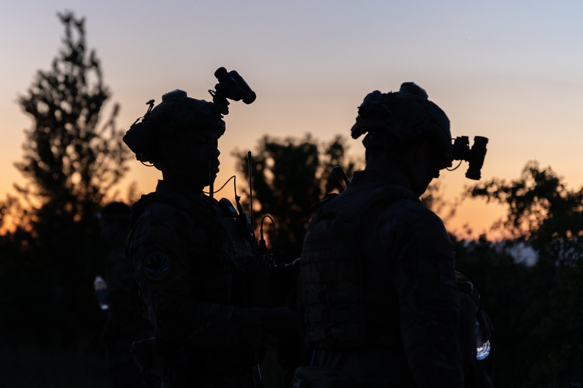 The silhouettes of two Airmen wearing helmets and night vision goggles.