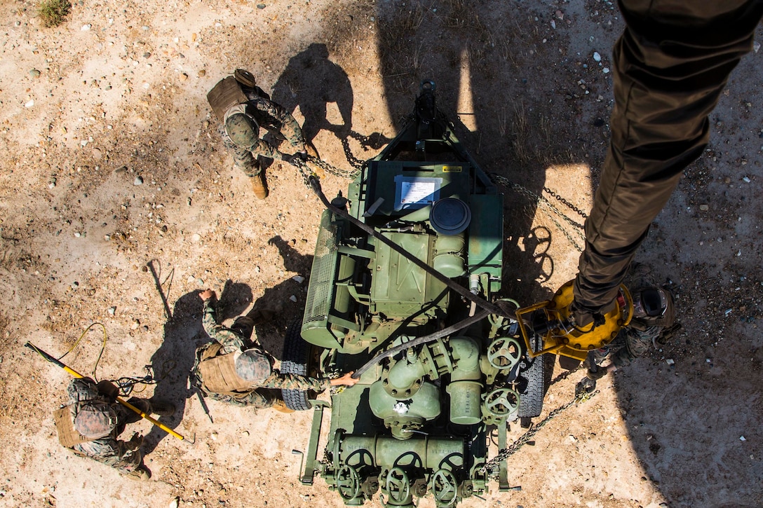 Marines attach equipment to a helicopter as shown from above.