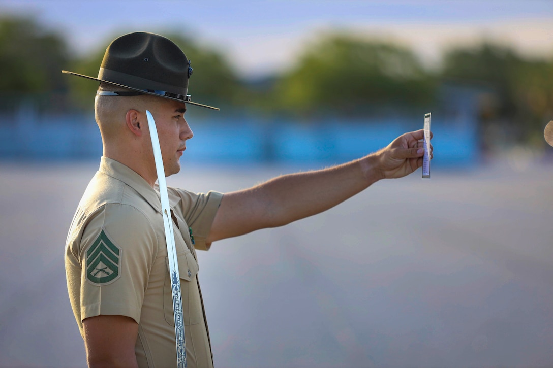 A Marine holds a piece of paper in one hand while holding a sword in the other.