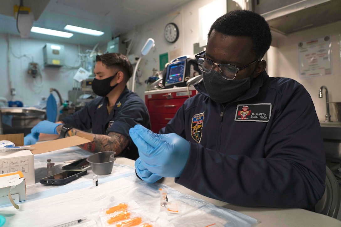 Two sailors prep vaccine samples at a table.