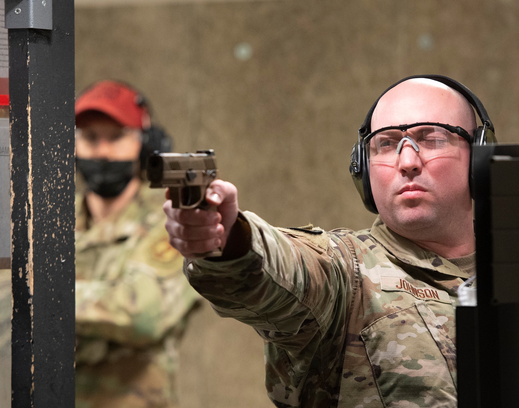 U.S. Air Force Tech. Sgt. Dakota Johnson, 88th Security Forces Squadron, takes aim with his M-18 in the squadron’s indoors shooting range on Wright-Patterson Air ForceBase, Ohio, May 11, 2021, as a combat arms instructor looks on. The squadron held a shooting competition as part of its annual Police Week activities. (U.S. Air Force photo by R.J. Oriez)