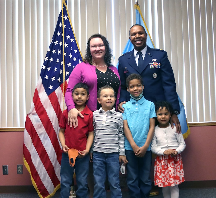 a military man in uniform stands with his wife and four kids
