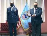 a military man in uniform stands at attention while man in civilian attire presents medal