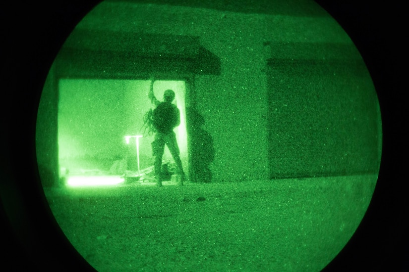 Seen through a night vision scope, a soldier opens the door of a storage facility.