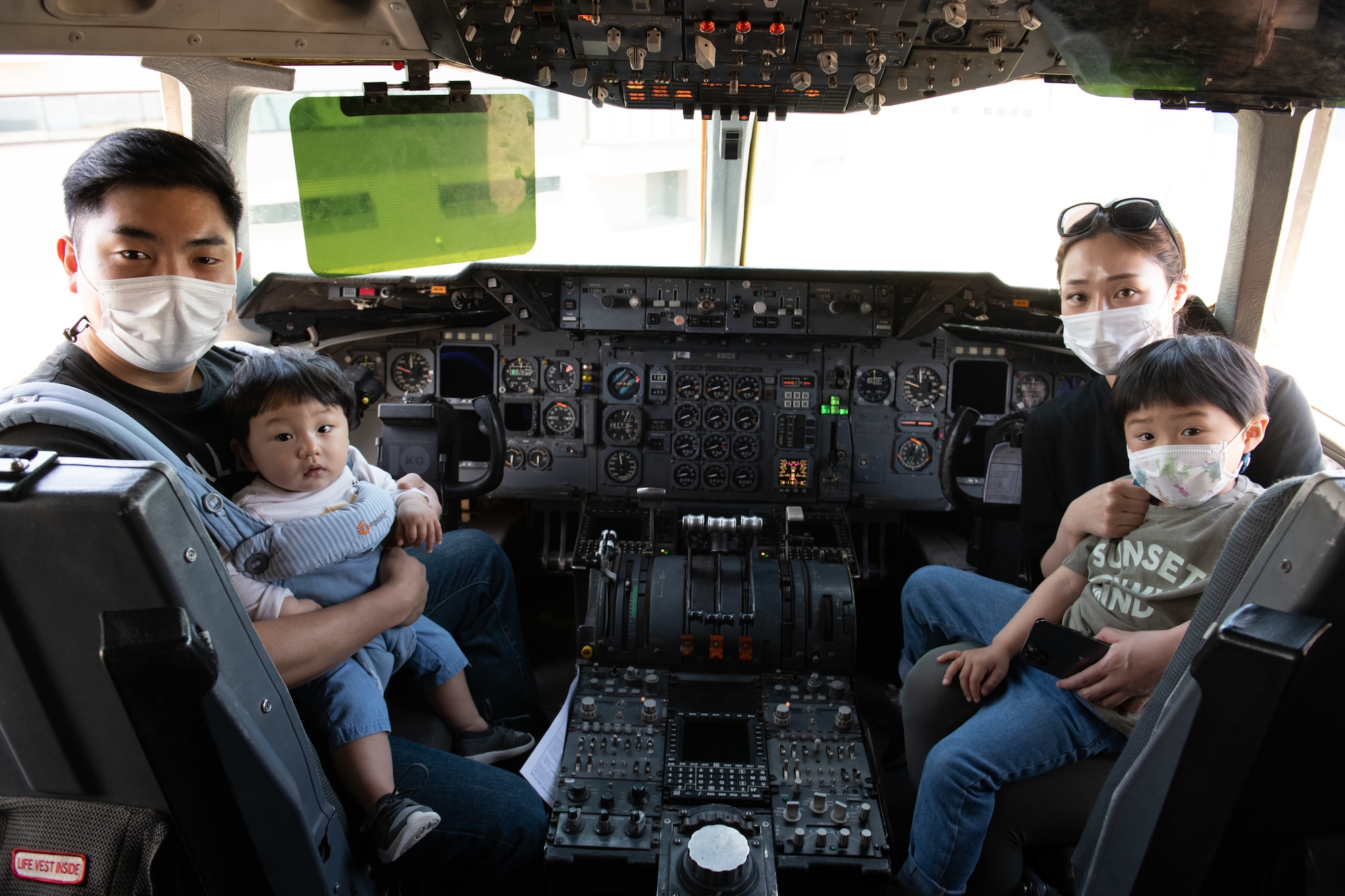 An Asian American family poses for a photo while sitting at the pilot seats of a KC-10 Extender.
