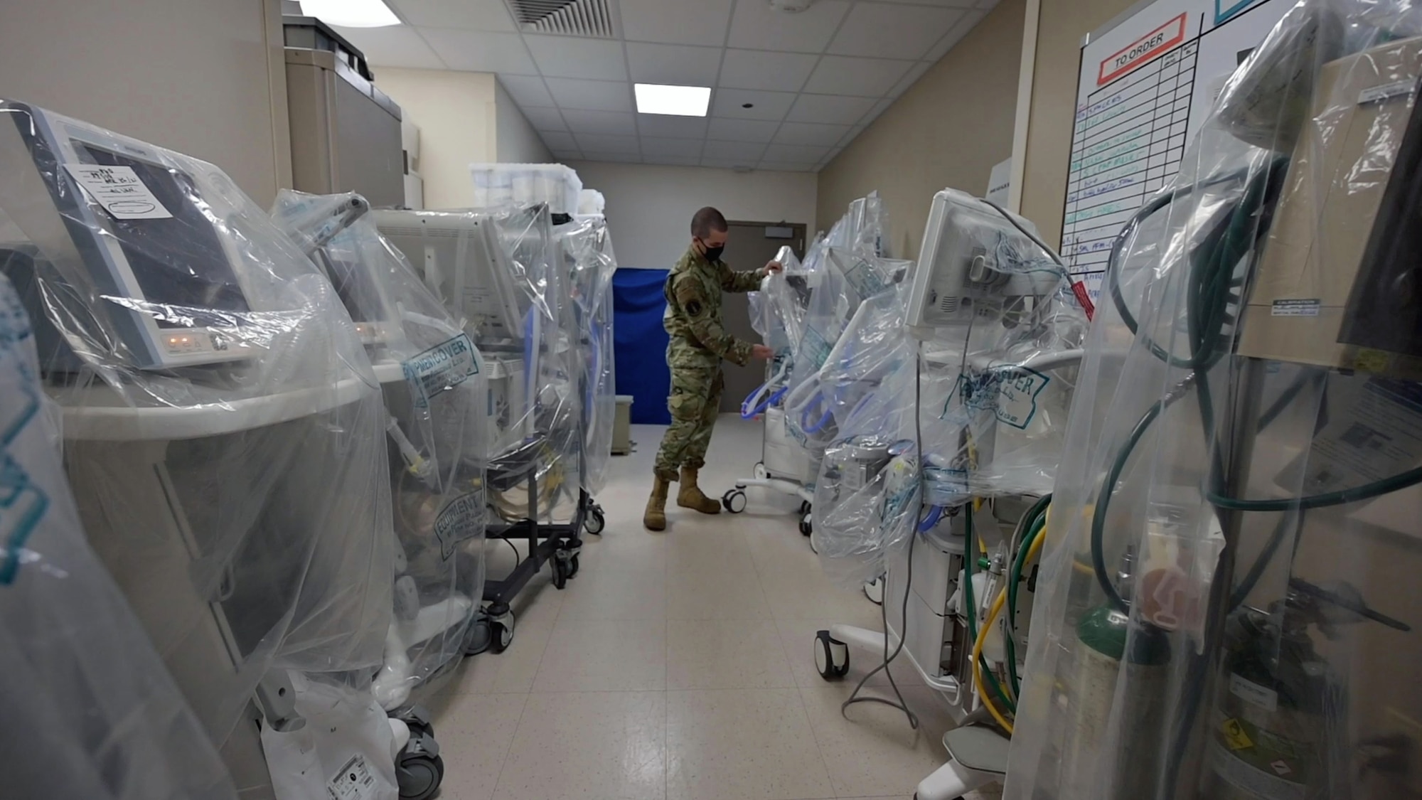 An Airmen walks through a row of ventilators covered in plastic.