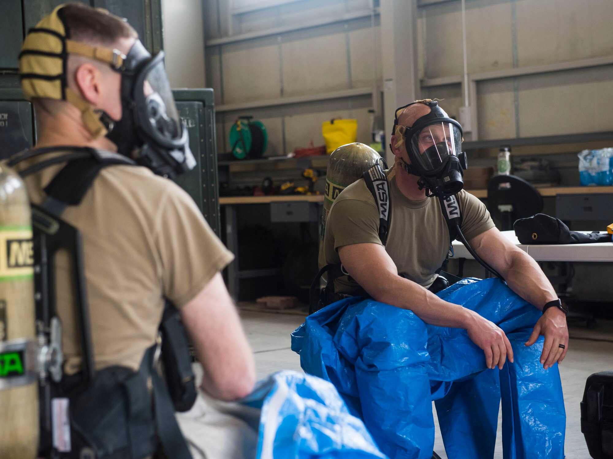 Two men wearing hazmat suits sitting on chairs.