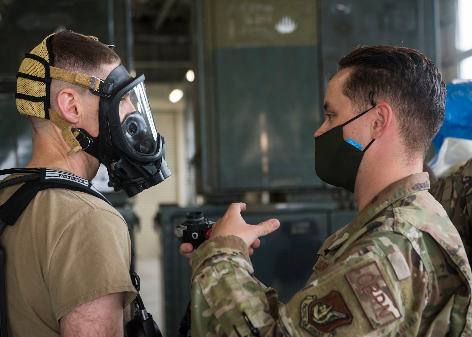 One man in uniform helps another man equip a oxygen mask.