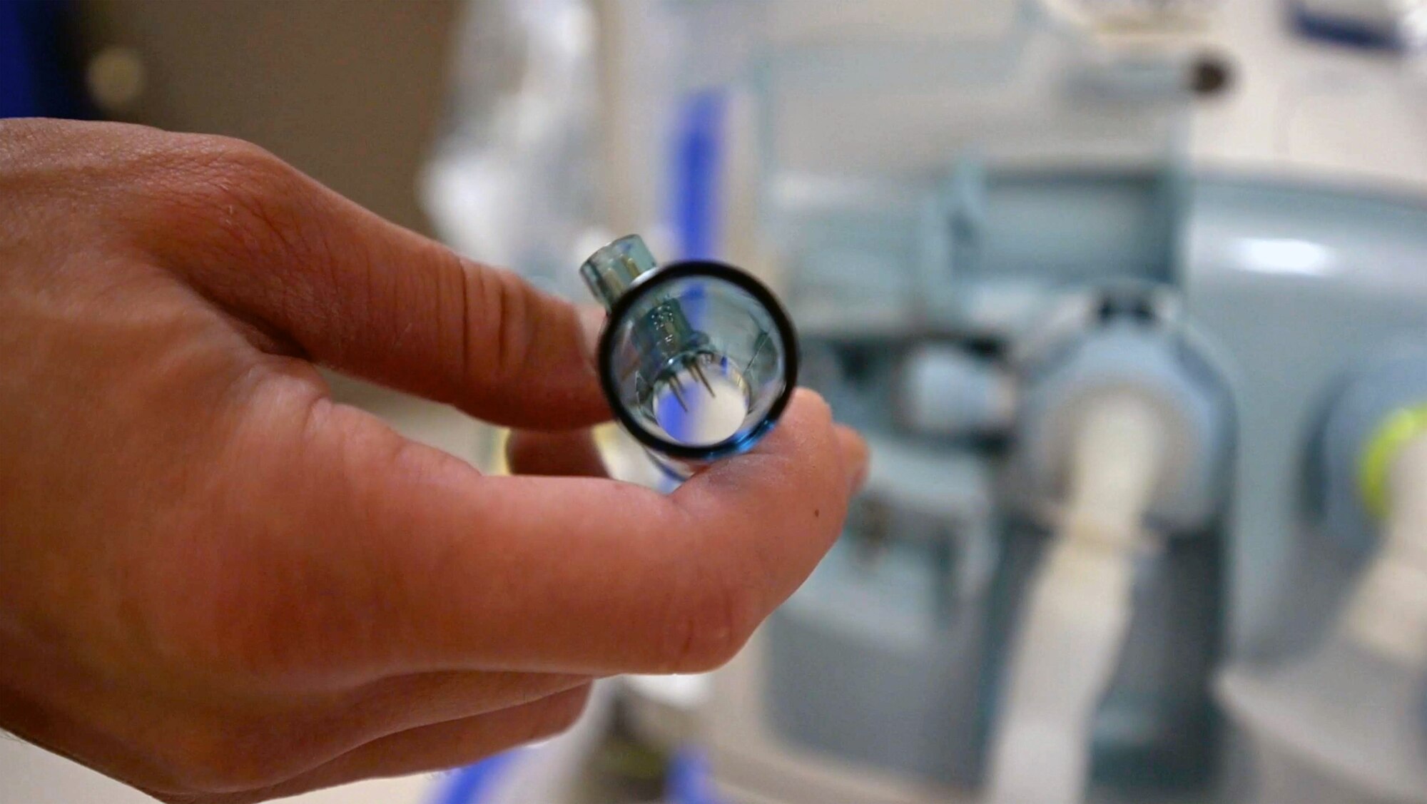 A man holds a small piece of blue plastic with wires inside.