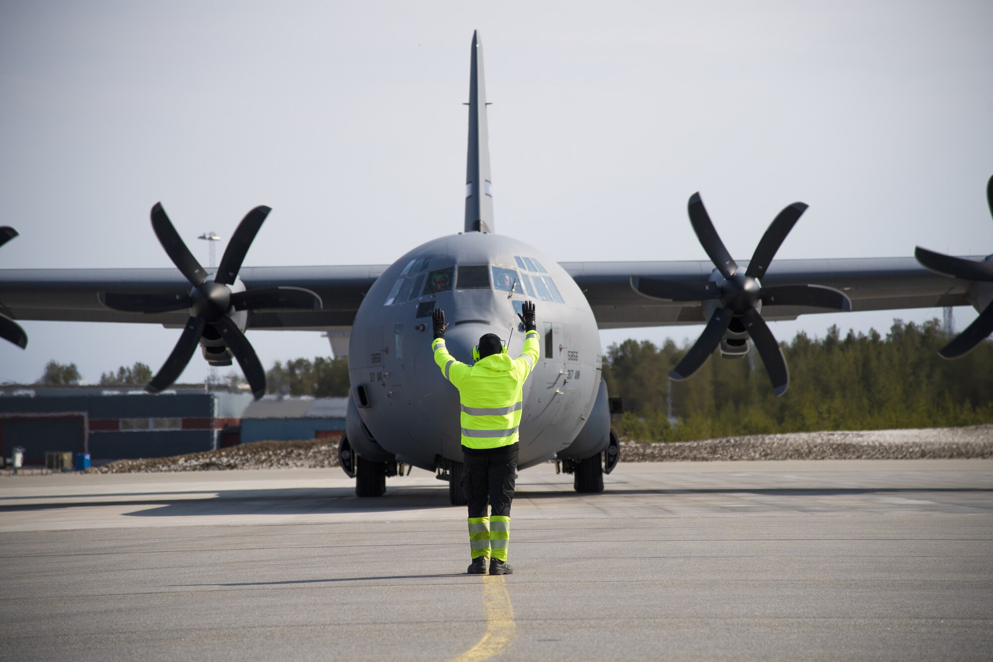 An employee at Kallax Air Base, Sweden, directs a U.S. Air Force C-130 Hercules aircraft on the taxiway at Kallax AB, Sweden, May 14, 2021. The aircraft transported supplies to be used in the Arctic Challenge Exercise 2021, as well as Airmen from the 52nd Fighter Wing at Spangdahlem Air Base, Germany, and the 86th Airlift Wing at Ramstein Air Base, Germany. (U.S. Air Force photo by Senior Airman Ali Stewart)