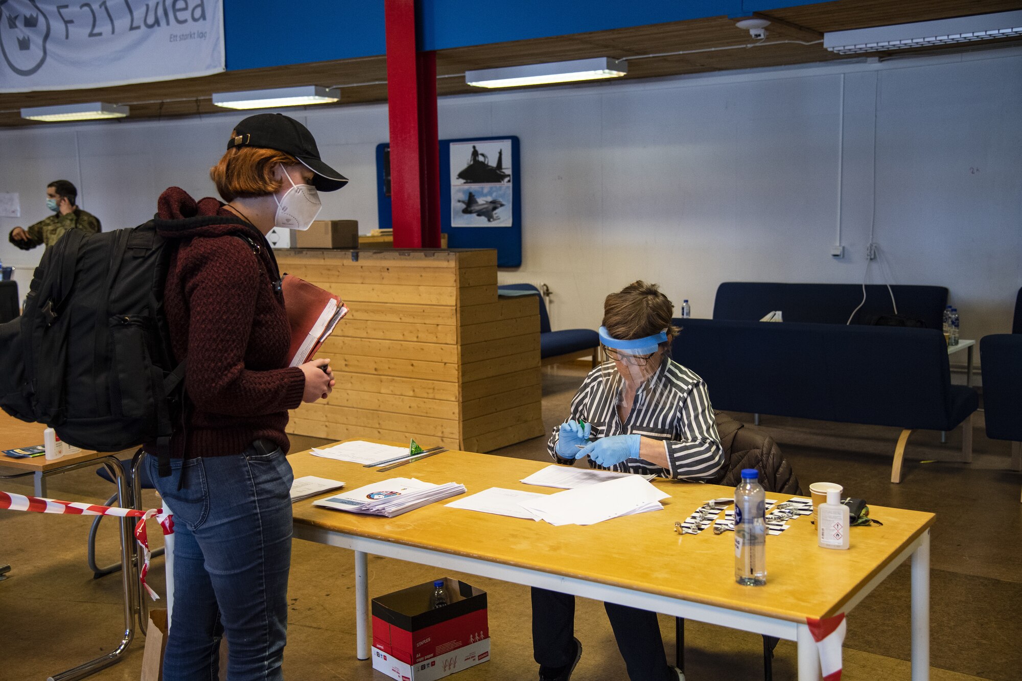 A U.S. Air Force Airman from Spangdahlem Air Base, Germany, left, presents paperwork to a Swedish border control employee at Kallax Air Base, Sweden, May 14, 2021. With the support of the Swedes, Airmen were able to safely in-process into the country while taking the proper COVID-19 safety measures, ensuring that the Arctic Challenge Exercise would be conducted in a safe and healthy environment. (U.S. Air Force photo by Senior Airman Ali Stewart)