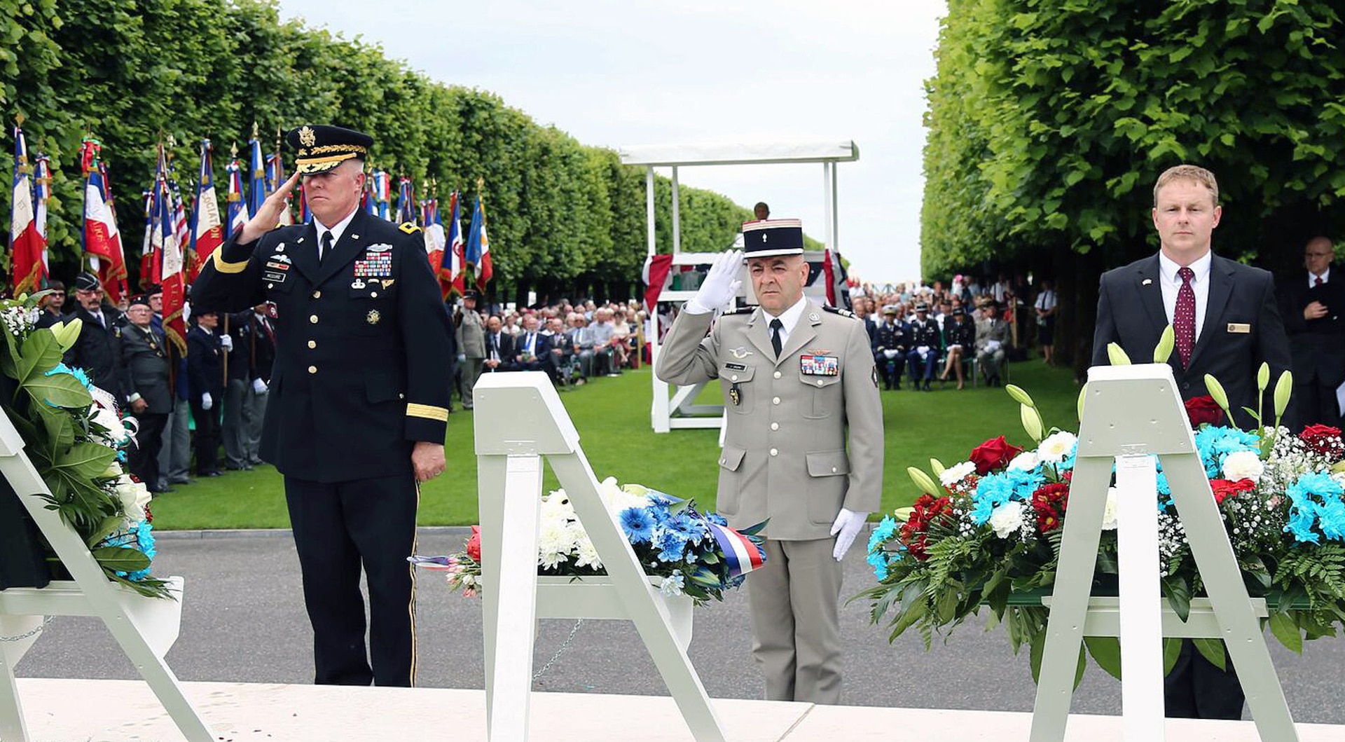 Three men standing in a cemetery. Two military members saluting.