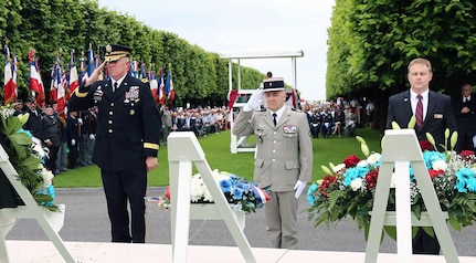 Three men standing in a cemetery. Two military members saluting.