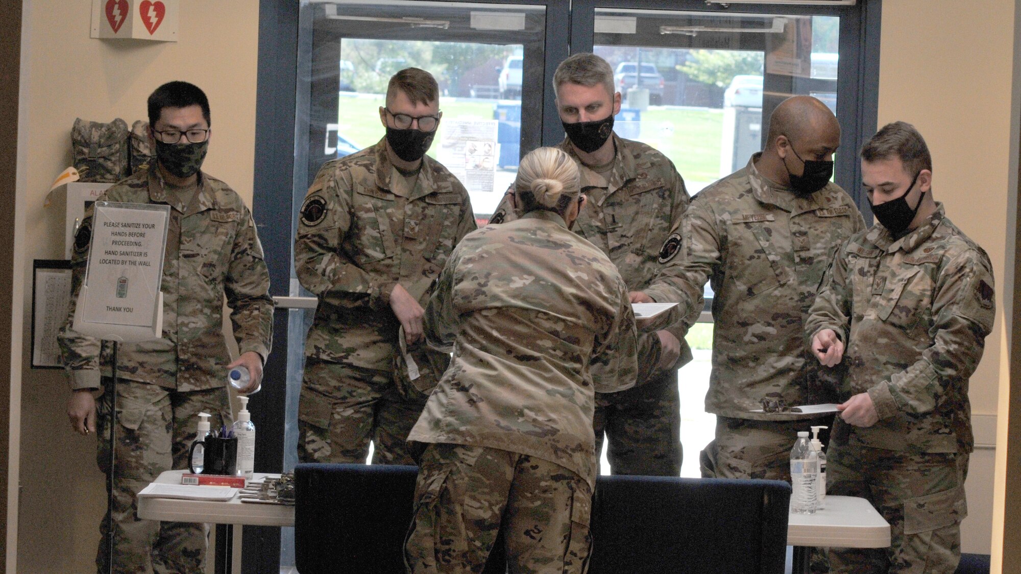 Airmen in uniform surrounding a desk where a female in uniform checks them in.