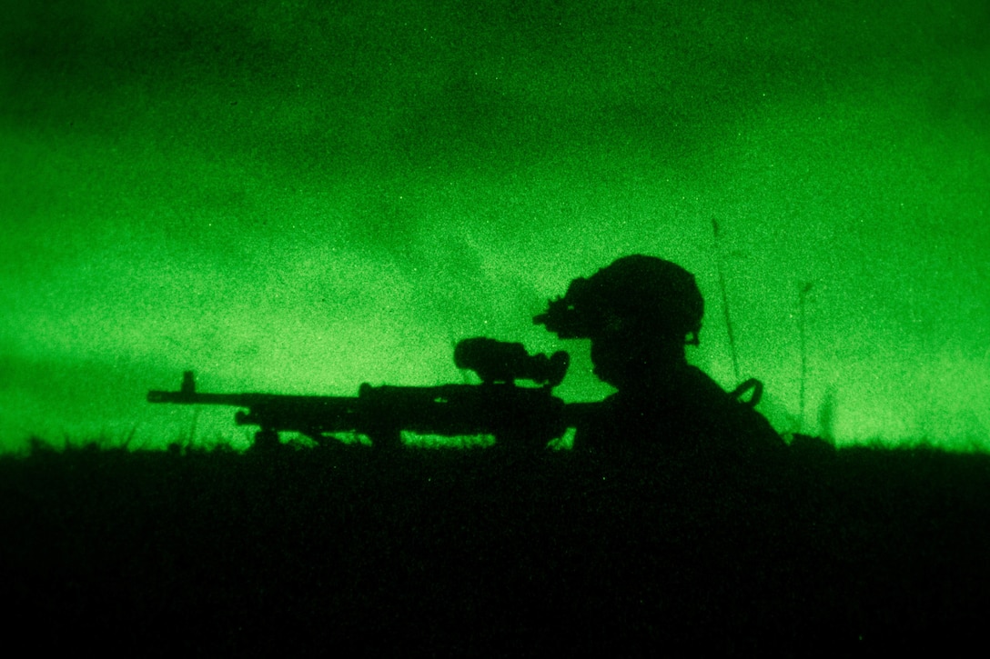 A Marine aims a weapon illuminated by green light.
