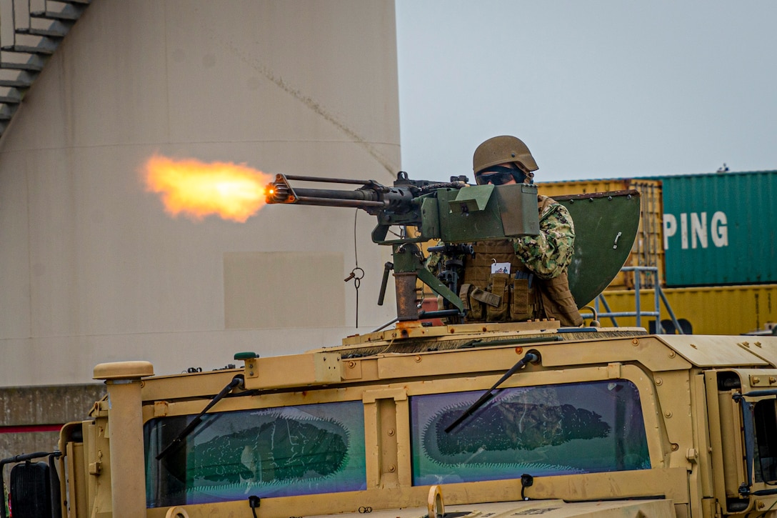 A sailor fires a machine gun from the top of a military vehicle.