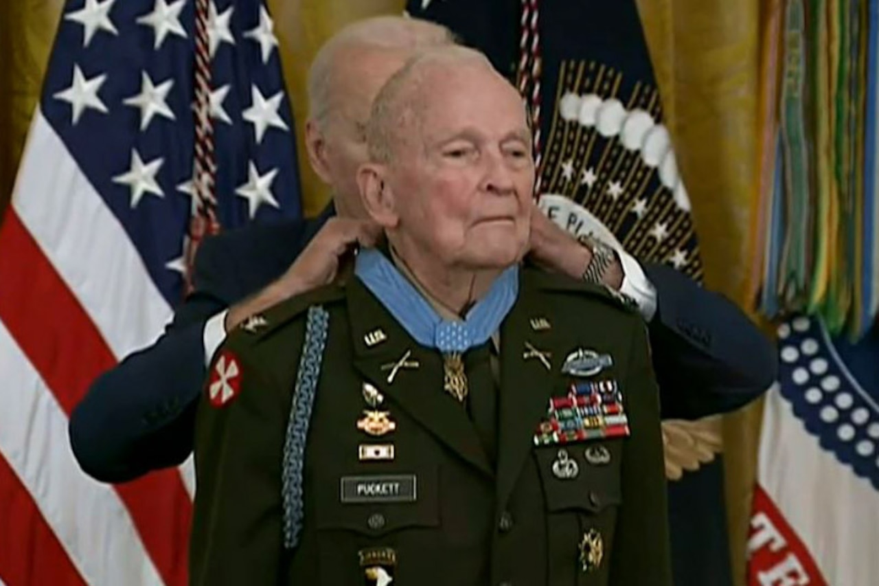 A man places a medal around the neck of another man in a military uniform.