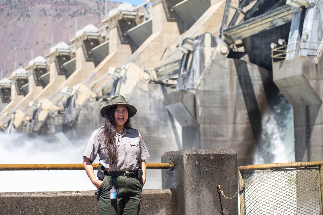 A ranger stands in front of a dam spillway.