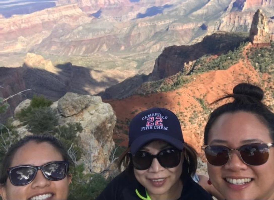 Three people stand together with a view of the Grand Canyon in the background.