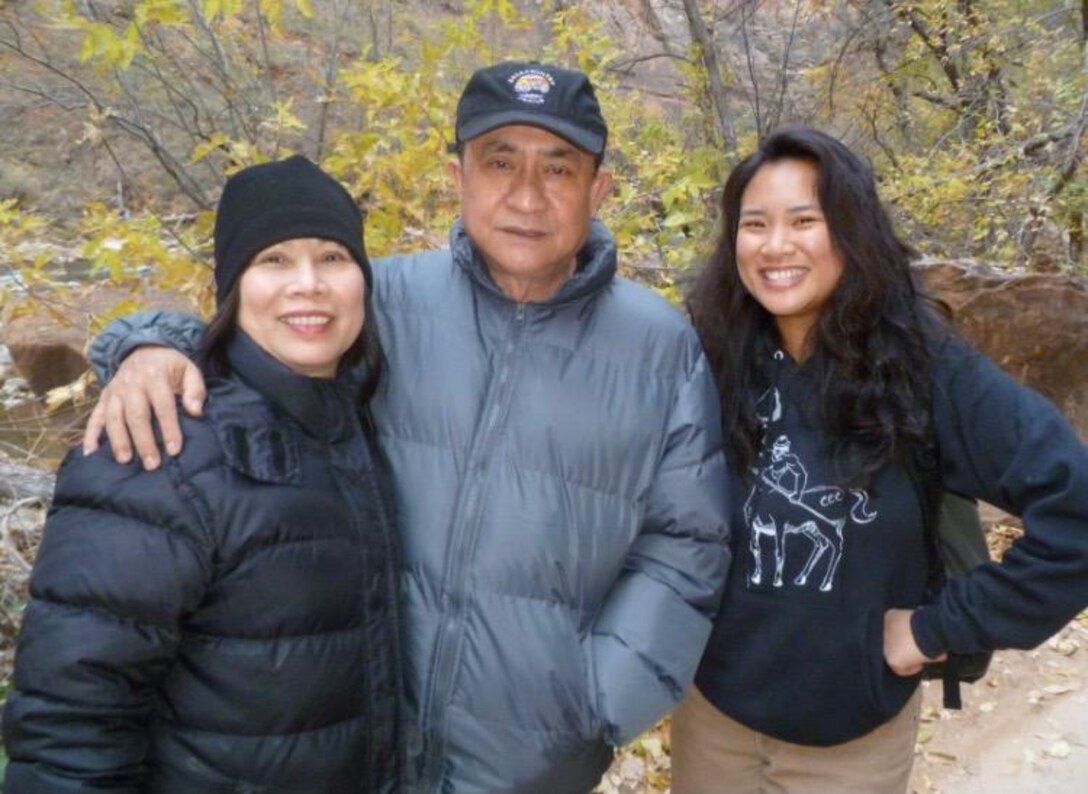 Three people stand together, smiling.