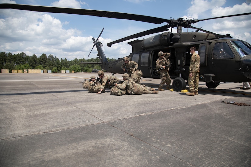 Troops practice drills next to a helicopter.