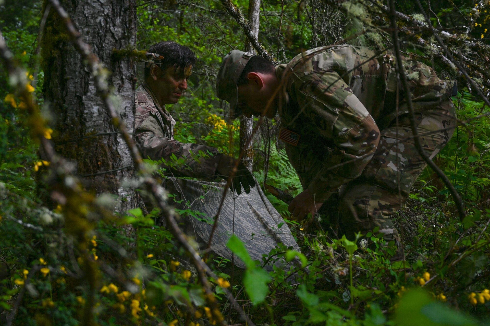 U.S. Soldiers assigned to Alpha Company 2-158 , 2nd Battalion, 158th Aviation Regiment, build an evasion shelter at Joint Base Lewis-McChord, Washington, May 18, 2021. 62nd Operations Support Squadron survive, evade, resist, and escape specialists hosted an evasion exercise for A Co 2-158, where they practiced evasion living utilizing fire, shelter and camouflage paint. (U.S. Air Force photo by Airman 1st Class Callie Norton)
