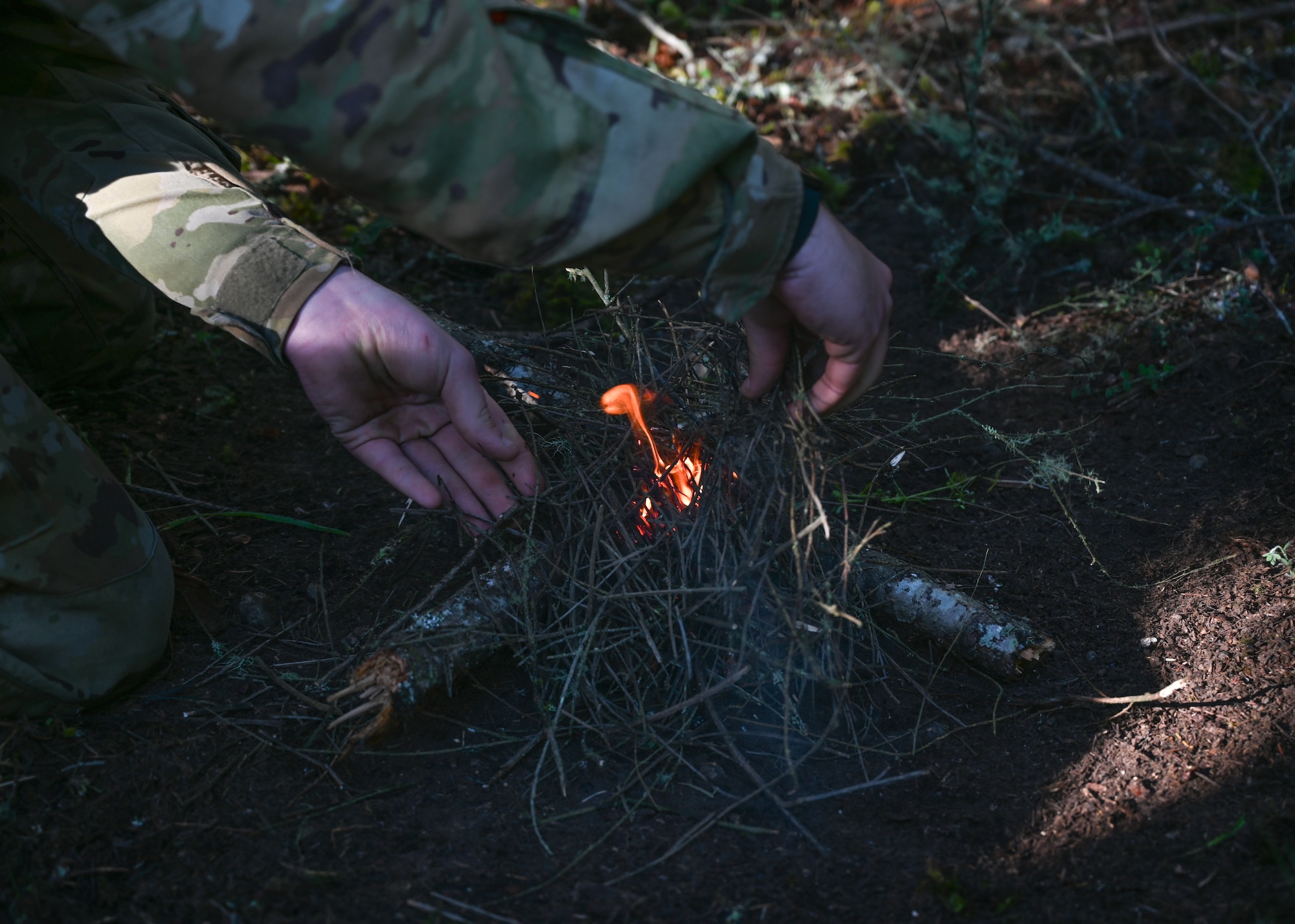 A U.S. Soldier assigned to Alpha Company 2-158 , 2nd Battalion, 158th Aviation Regiment, starts an evasion fire at Joint Base Lewis-McChord, Washington, May 18, 2021. 62nd Operations Support Squadron survive, evade, resist, and escape specialists hosted an evasion exercise for A Co 2-158 where they practiced evasion living utilizing fire, shelter and camouflage paint. (U.S. Air Force photo by Airman 1st Class Callie Norton)