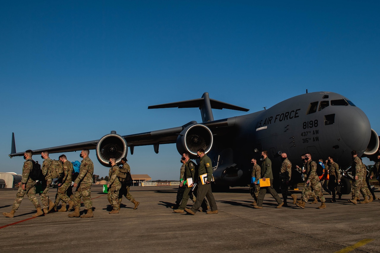 A group of airmen file past an aircraft.