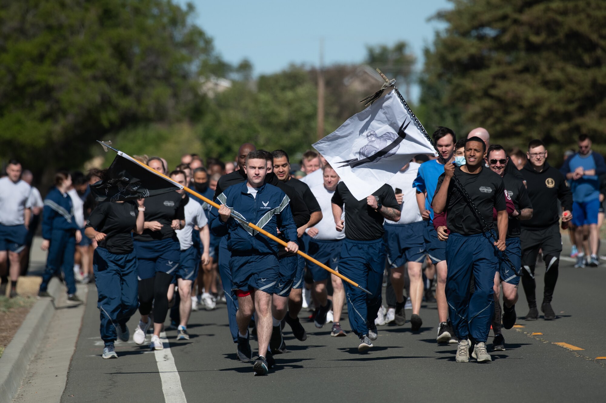 A group of people wearing workout gear are running towards the camera and the front two people are holding flags. Each flag has a symbol recognizing today's holiday and the remembrance run.