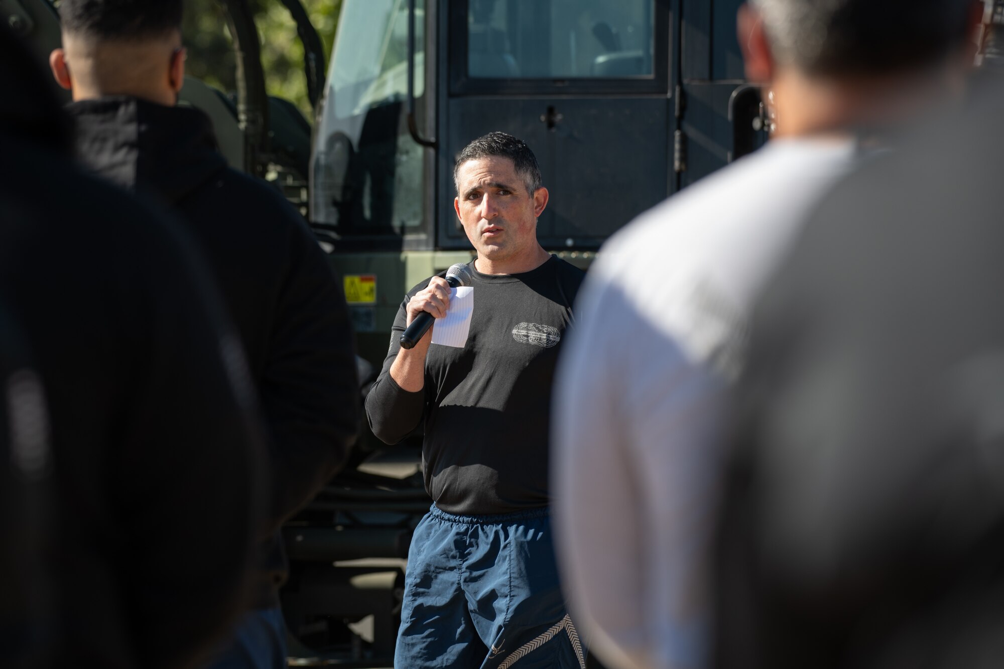 A man in workout gear speaks into a microphone in front of a group of people.