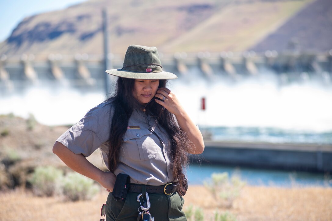 A ranger stands with a dam in the background.