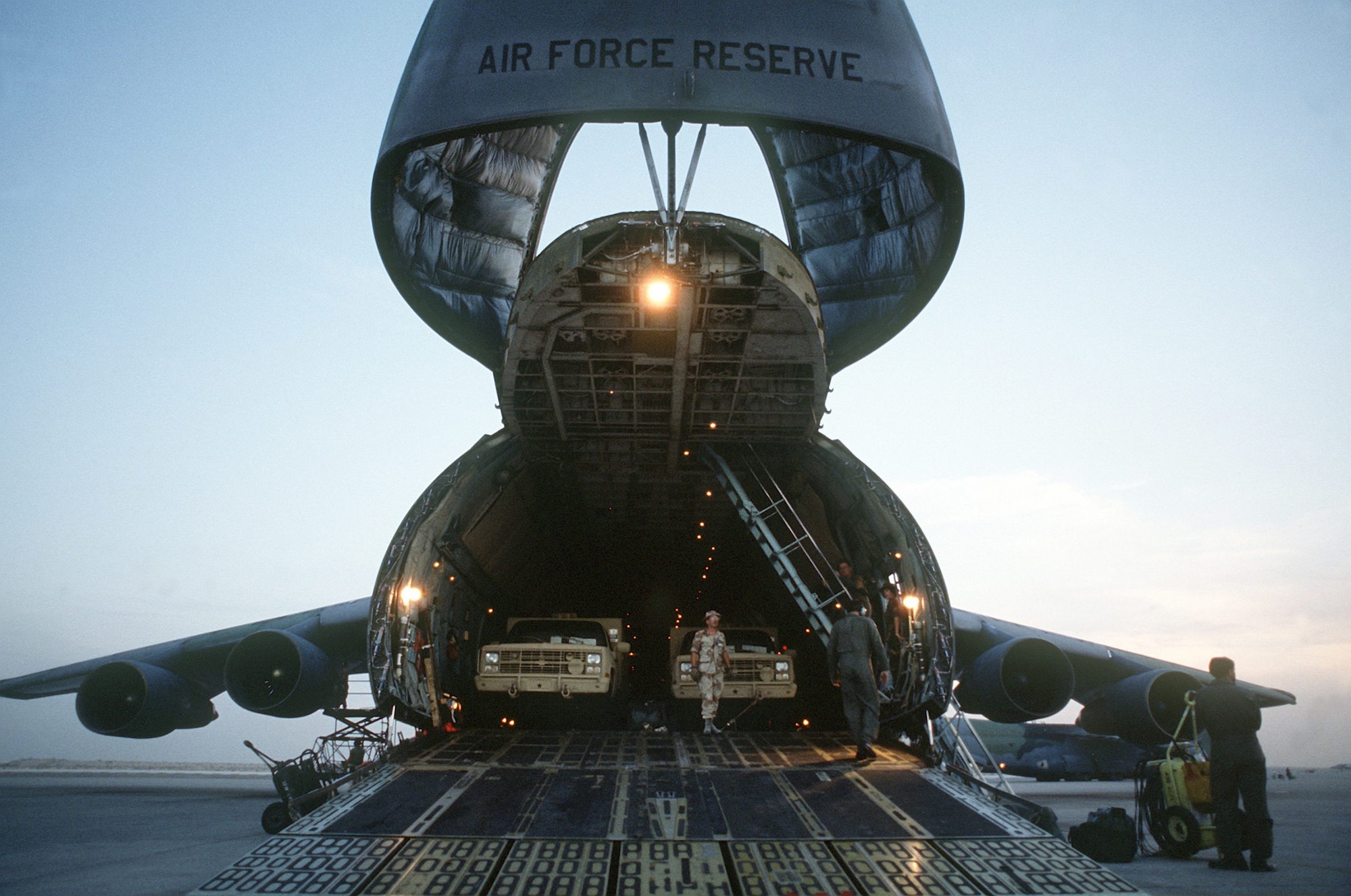 Military trucks are unloaded from the nose ramp of a C-5A Galaxy transport aircraft of the U.S. Air Force Reserve, Military Airlift Command, in support of Operation Desert Shield.