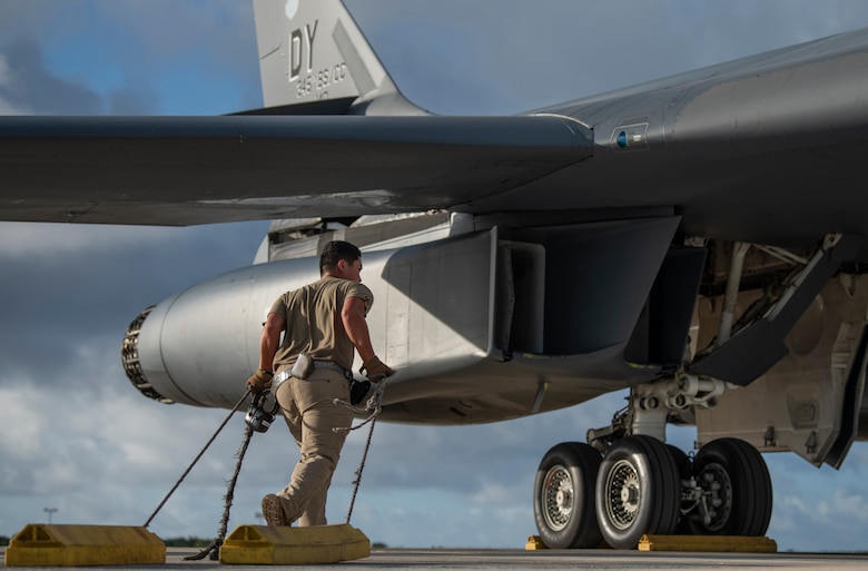 Senior Airman Jae Sajonas, 9th Expeditionary Bomb Squadron B-1B Lancer assistant crew chief, drags wheel chocks on the flightline at Andersen Air Force Base, Guam, May 14, 2020. Chocks prevent the aircraft from moving or swaying. Approximately 200 Airmen and four B-1s assigned to the 7th Bomb Wing at Dyess AFB, Texas, deployed to support Pacific Air Forces' training efforts with allies, partners and joint forces; and strategic deterrence missions. (U.S. Air Force photo illustration by Senior Airman River Bruce)