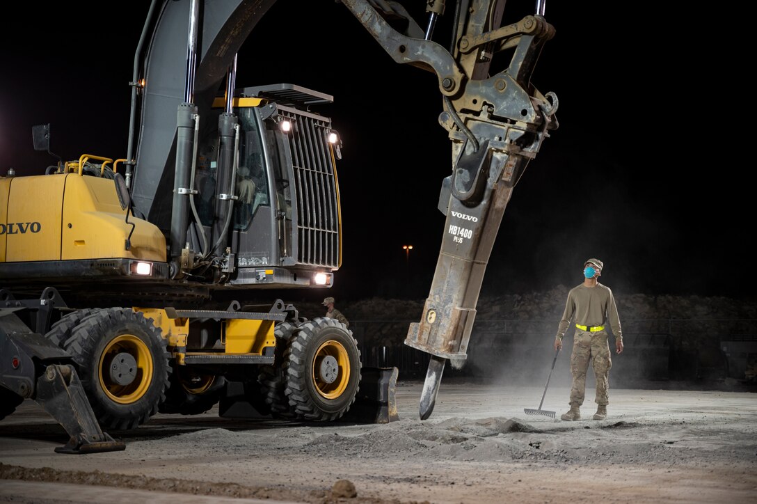 An Airmen stands next to a large construction vehicle.