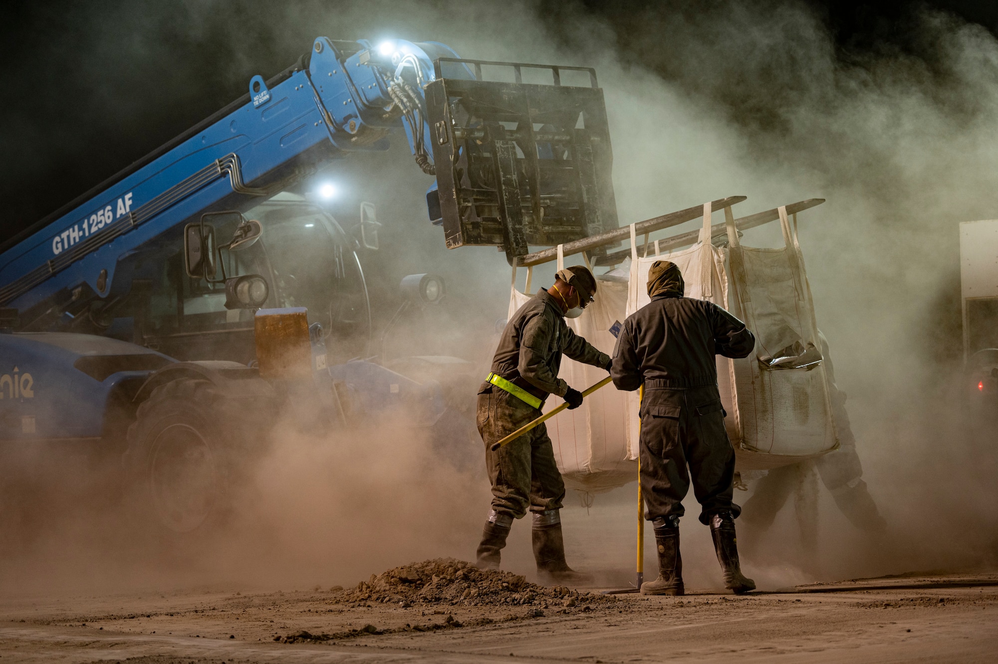 Airmen wearing protective gear fill a hole with dry concrete powder.
