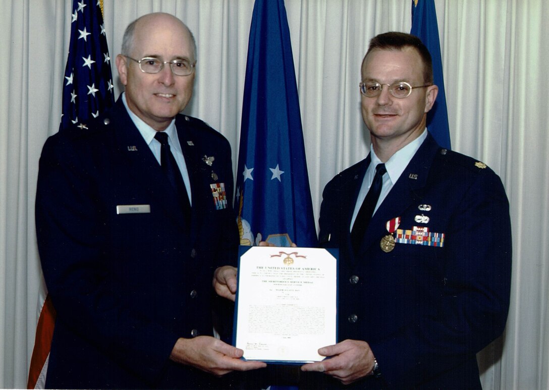 Two man in dress uniforms stand in front of the US and DLA flags holding a certificate.