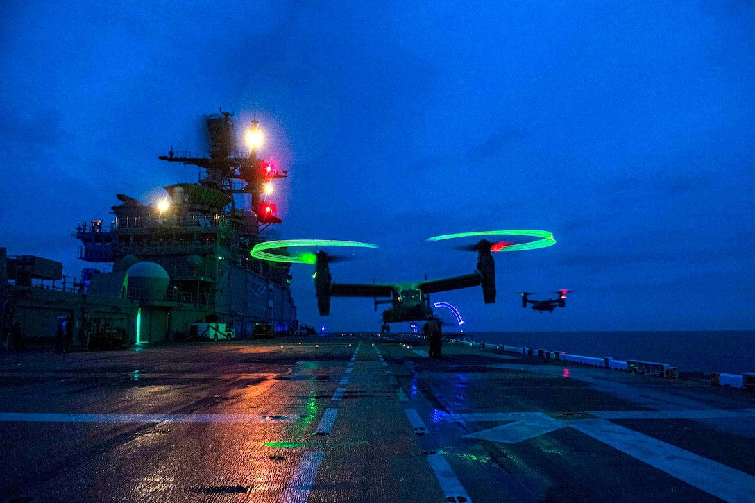 A military aircraft lands on a ship in the dark.