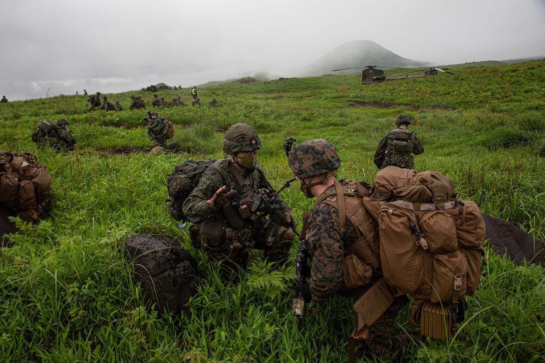 Service members kneel in a large grassy field on a foggy day.