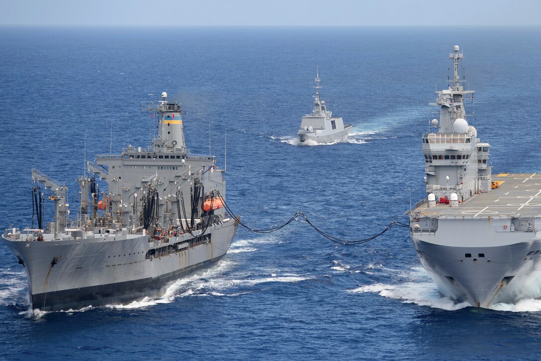 A ship refuels another ship while a small boat follows along.