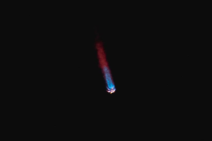 A rocket with a blue and red tail flies through a black sky.