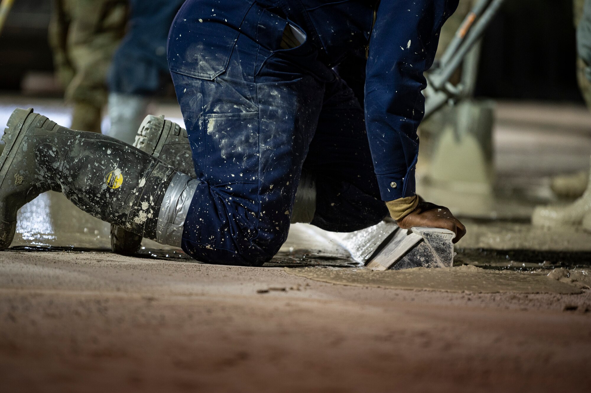 An Airman applies pressure to a vibratory screen over drying cement to level it.