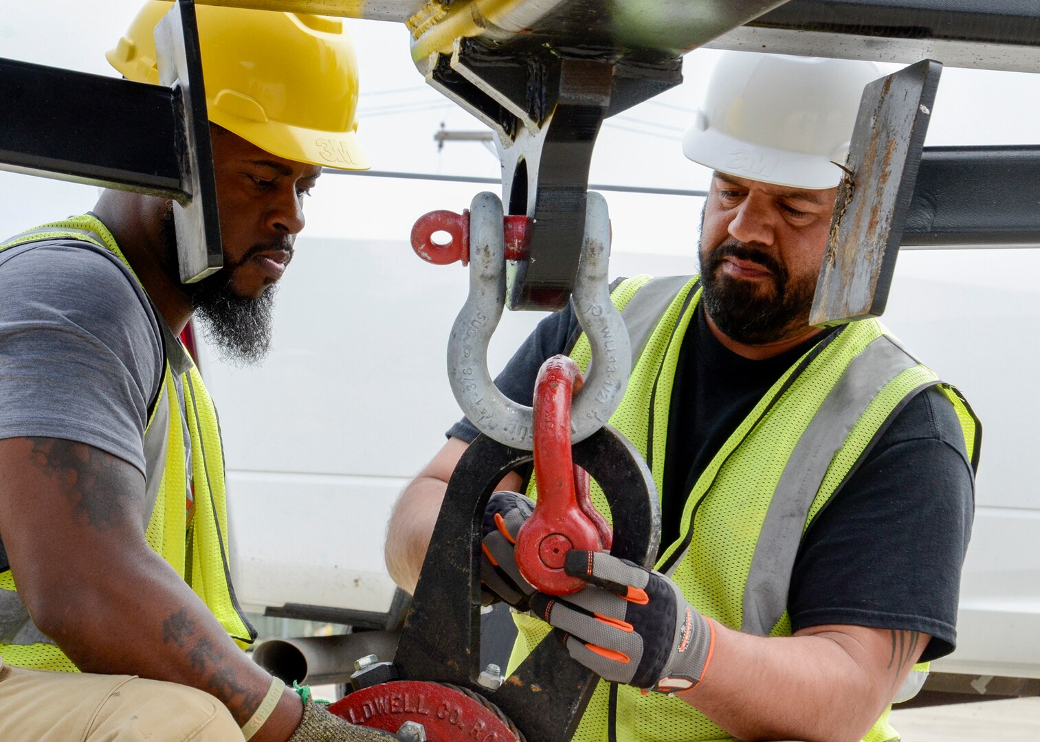 Two men hook up a sling for heavy equipment lifting.