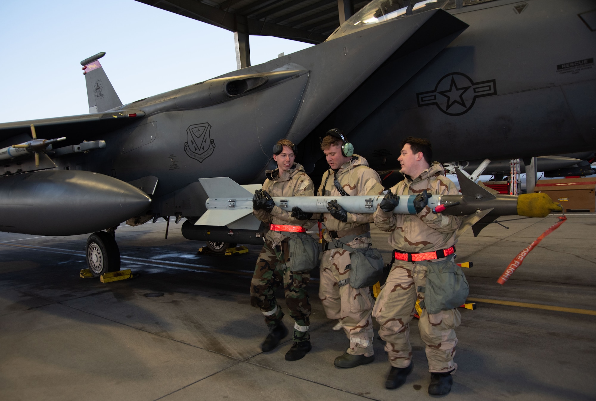 Three Airmen from the 389th Fighter Squadron lifts and transports an Air Intercept Missile to a F-15E Strike Eagle.