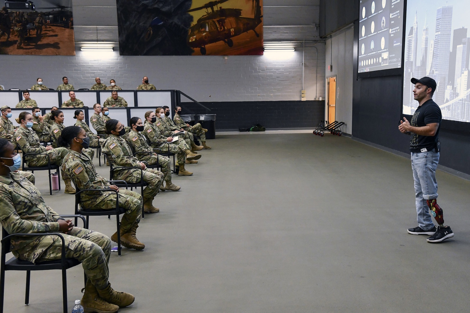 Man with prosthetic leg speaks to soldiers.