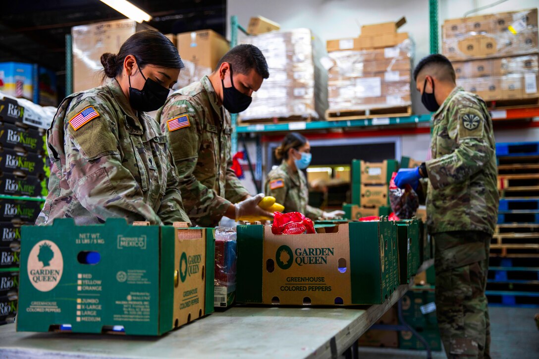 Soldiers wearing face masks and gloves fill boxes with fresh produce at a local food bank.